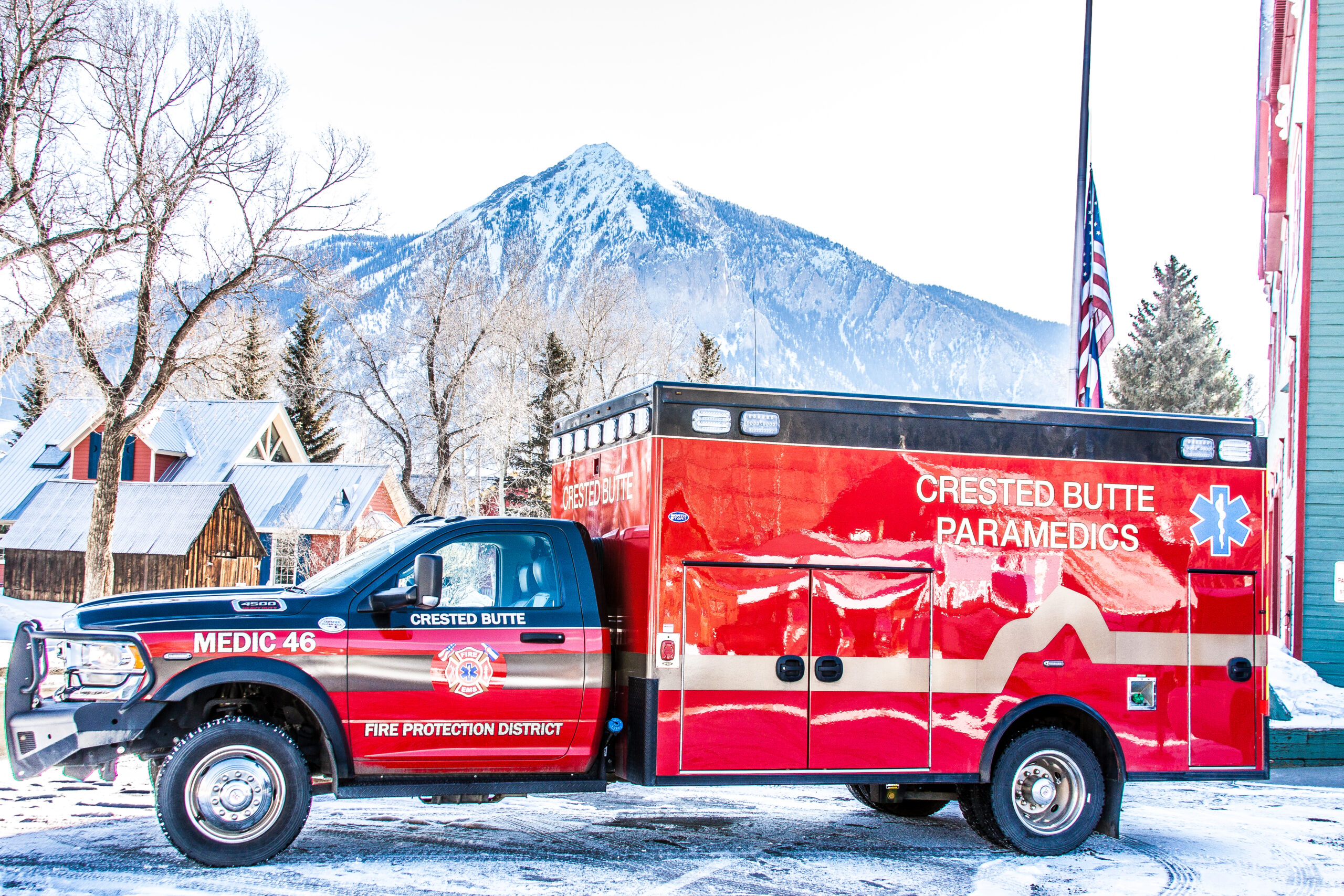 Photo of CBFPD Medic 46. A red and gray ambulance parked in front of a snow covered mountain.